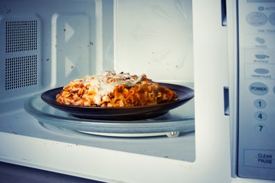 A plate of leftover lasagna is reheated in a microwave.