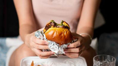 Woman eating fast food meal of burger and fries delivered at home alone