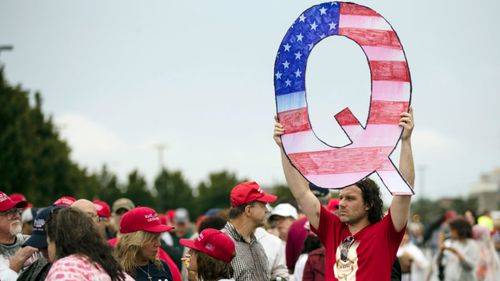 A protester holding a Q sign waits with others at a campaign rally held by then President Donald Trump.