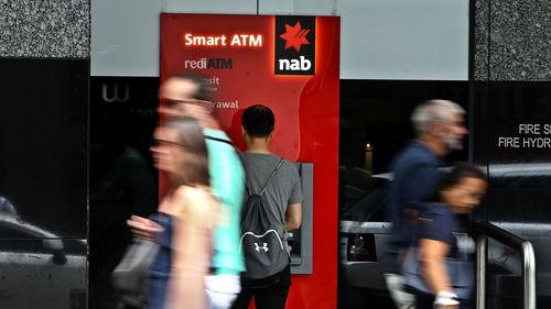 A man uses an NAB ATM as pedestrians walk past.