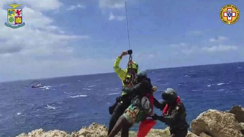 In this picture taken from video, a migrant stranded on a rocky reef on the tiny Italian southern island of Lampedusa, Sicily is plucked to safety by helicopter. 