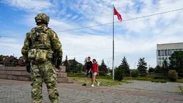A young couple walks past a Russian soldier guarding an area at the Alley of Glory in Kherson.