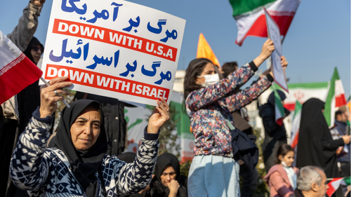 People hold placards and wave flags during a pro-government demonstration on January 12, 2026 in Tehran, Iran. 