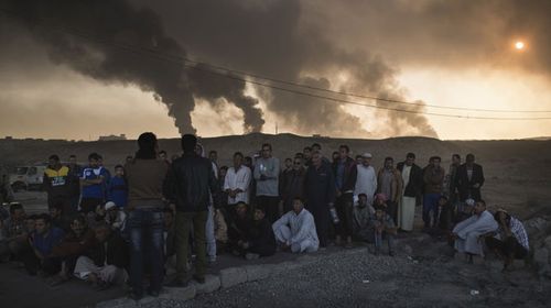 Men are held by Iraqi national security agents, to be interrogated at a checkpoint, as oil fields burn in Qayara, south of Mosul. (AAP)