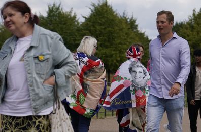 Two women wear flags with the likeness of Princess Diana as they walk outside the gates of Kensington Palace, in London, Wednesday, August 31, 2022.  