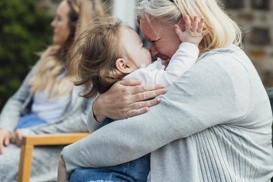 A shot of a senior woman embracing her granddaughter and laughing. They are wearing casual clothing and are sitting in a garden at a baby shower.