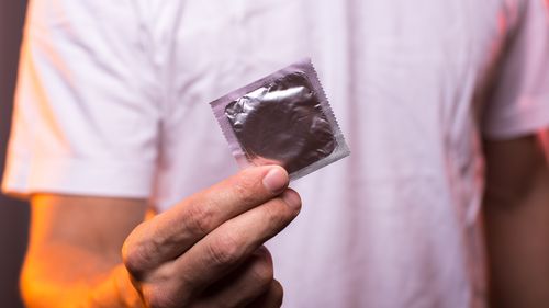 Unknown man in white shirt holding condom in hand, closeup. Safety sex concept.