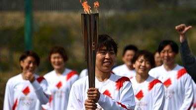 Azusa Iwashimizu (L), member of Japan women's football national team, lights the torch from the celebration cauldron during the Tokyo 2020 Olympic Torch Relay Grand Start. (Getty)