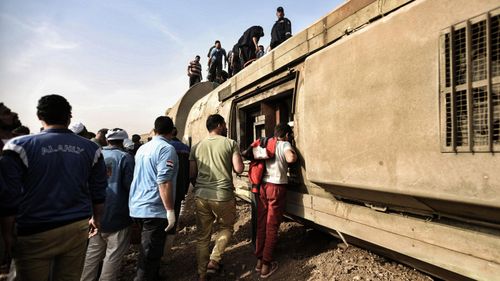People inspect the damaged wagons of a passenger train, which went off the tracks near Toukh.