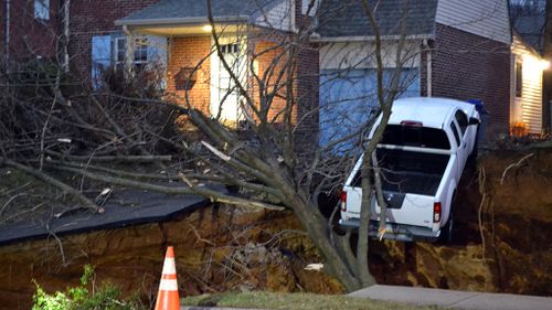 A giant sinkhole has swallowed up two front gardens in Philadelphia and a pick-up truck is teetering on the edge of the crater. (AAP)