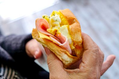 Close up mature woman eating egg sandwich with ham & Cheese for breakfast meal