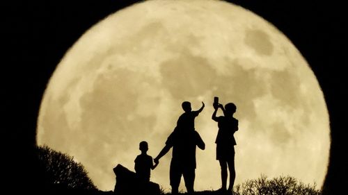 A family stand with the full moon known as the "Sturgeon Moon"