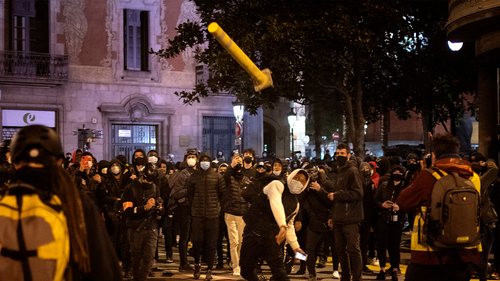 A man throws a road sign agains police officers protecting a national police station during clashes following a protest condemning the arrest.