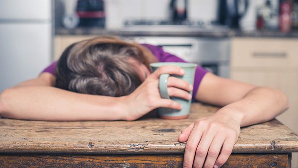 Person slumped on wooden desk holding a mug