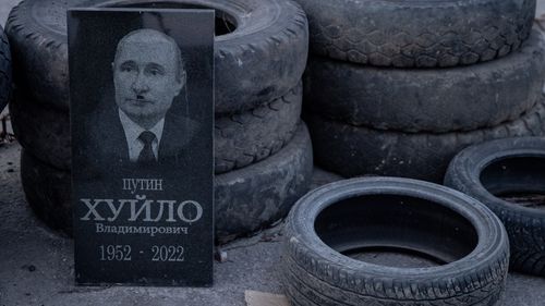 A grave stone showing the portrait of Russian President Vladimir Putin changed to look like Adolf Hitler is seen against a tyre barricade at a Ukrainian army checkpoint. 