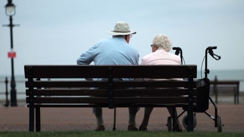A retired man and woman sit on a park bench.