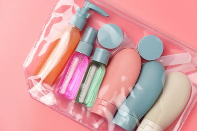 Clear plastic bag with travel size toiletries on pink background close-up