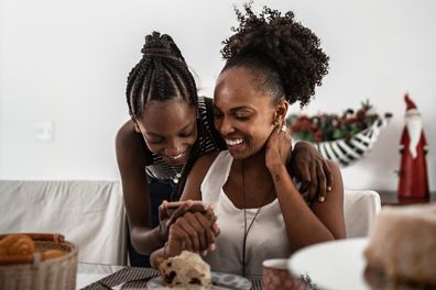 Teenager girl showing something on smartphone to mother during breakfast at home