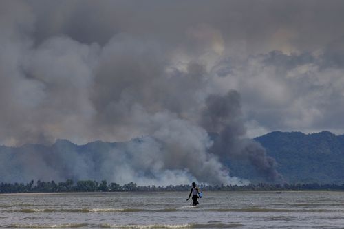 A Bangladeshi boy walks towards a parked boat as smoke rises from across the border in Myanmar. (AP)
