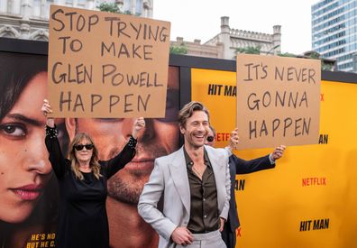 Glen Powell's parents hold up signs behind him as they attend the special screening of Hitman in Austin, Texas on May 15.