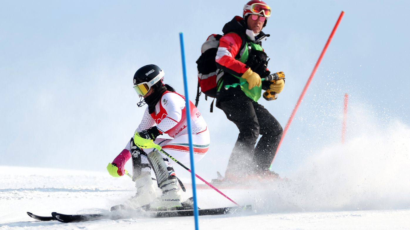 Eva Vukadinova of Team Bulgaria skis her run while a course worker is still repairing a broken gate during the Women&#x27;s Slalom Run 1 at the Beijing 2022 Winter Olympic Games.
