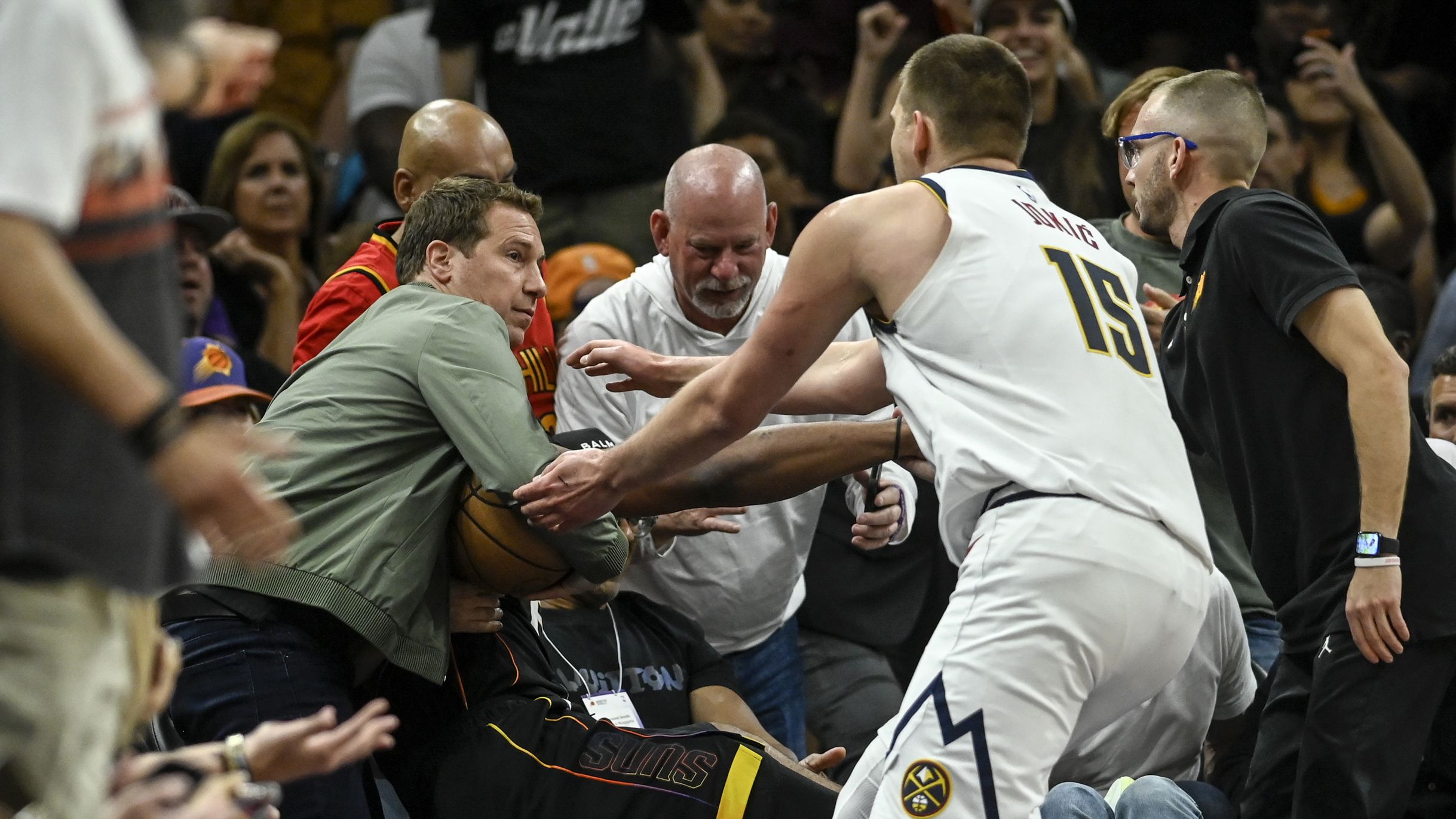 PHOENIX, AZ - MAY 7: Nikola Jokic (15) of the Denver Nuggets rushes to retrieve the game ball as Phoenix Suns owner Mat Ishbia inserts himself into the action by clutching the ball as he helps Josh Okogie (2) to his feet after Okogie flew into the stands during the second quarter at Footprint Center in Phoenix on Sunday, May 7, 2023. (Photo by AAron Ontiveroz/The Denver Post)
