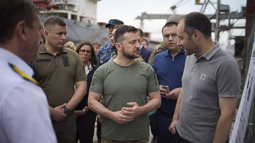 In this photo provided by the Ukrainian Presidential Press Office, Ukrainian President Volodymyr Zelenskyy, center, surrounded by ambassadors of different countries and UN officials, visits a port in Chornomork during loading of grain on a Turkish ship, background, close to Odesa, Ukraine, Friday, July 29, 2022. (Ukrainian Presidential Press Office via AP)