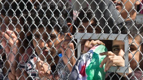 Migrants and refugees stand behind a locked metal door as Pope Francis and Ecumenical Patriarch Bartholomew I visit the Moria refugee detention center on the Greek island of Lesbos. (AAP)