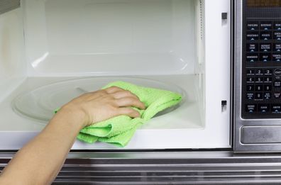 Hand with microfiber cleaning rag wiping inside of microwave oven