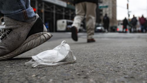 A used protective face mask rests on the pavement as pedestrians pass, Tuesday, March 17, 2020, in New York. 