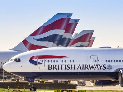 Boeing 777 long haul airliner operated by British Airways taxiing for take off at London Heathrow Airport past tail fins of the company's other aircraft.