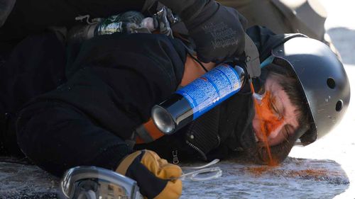 An ICE agent sprays pepper spray directly into the eyes of a protester who is pinned to the ground.