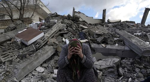 A woman sits on the rubble as emergency rescue teams search for people under the remains of destroyed buildings in Nurdagi town on the outskirts of Osmaniye city southern Turkey.