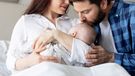 Father kissing his newborn baby at the hospital while mother holds him