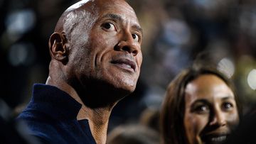Dwayne &#x27;The Rock&#x27; Johnson stands on the sideline in a football game.