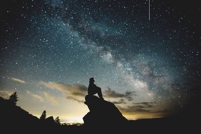 Person sitting on a rock looking at the stars.