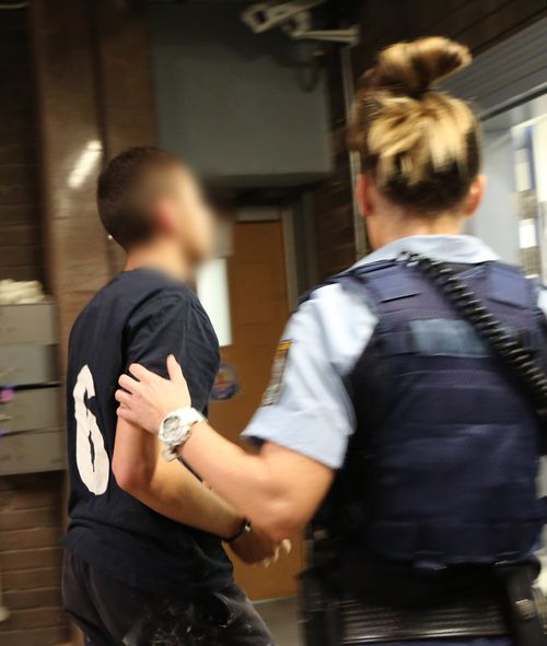 Police leading one of the accused into the station. (NSW Police Force)