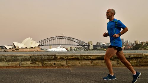 A man runs by the harbourside a day after strong winds blew the cloud in from the NSW interior.