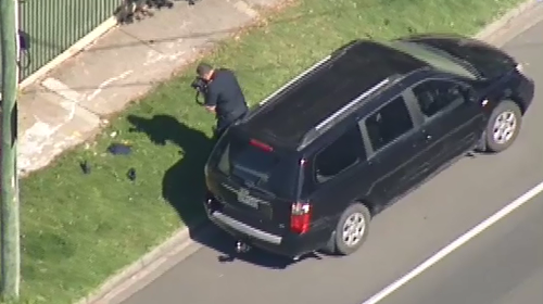 A detective takes a photo of shoes next to the black Kia Carnival, after the child was taken to hospital. (9NEWS)