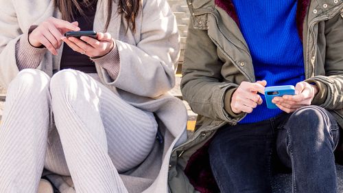 three unrecognizable friends sitting in the floor scrolling together through social media with mobile phone, concept of friendship and modern lifestyle