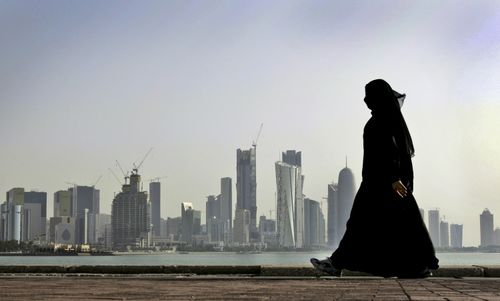 A Qatari woman walks in front of the Doha skyline. (AAP)