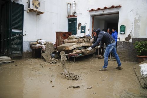 在意大利南部伊斯基亚岛的卡萨米乔拉，大雨导致山体滑坡导致建筑物倒塌，导致多达 12 人失踪，一名男子在房屋前清除泥土。