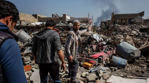 Residents in Mosul wade through rubble after a coalition air strike in 2017.