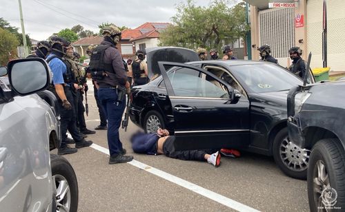 Diversi agenti di polizia pesantemente armati circondano un veicolo e un uomo arrestato nel sud-ovest di Sydney.