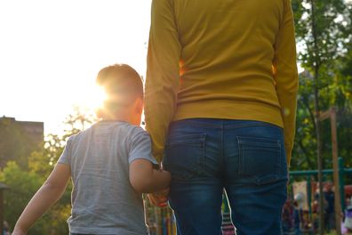 Child holding hands with her parent in nature at sunset.