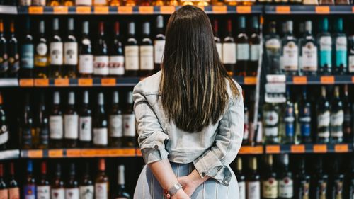 Vista traseira de uma cliente olhando para uma prateleira de vinho no supermercado