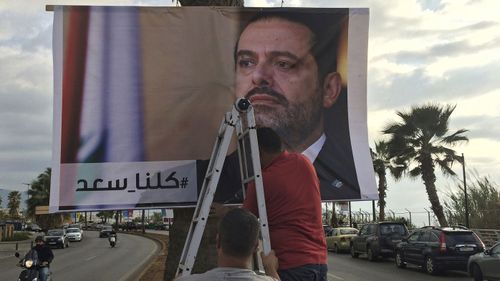 Workers hang a poster of outgoing Prime Minister Saad Hariri with Arabic words that read, "We are all Saad," at a seaside street in Beirut, Lebanon. (AP)