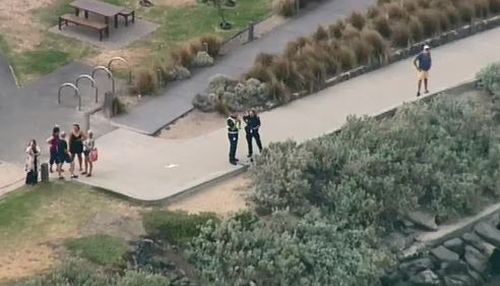 Officers stand on the shore while water police undertake a recovery operation.