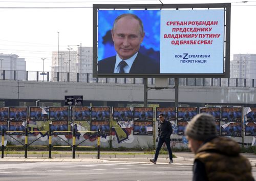 People walk past a big screen showing Russian President Vladimir Putin and reading: "Happy birthday to President Vladimir Putin from the Serb brethren!", in Belgrade, Serbia, Friday, Oct. 7, 2022. 
