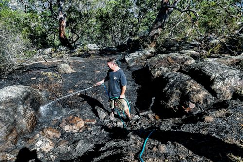 Justin Frith hoses down an area behind his home in Menai. (AAP)